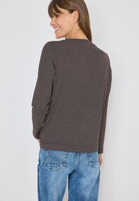 Maglione a maniche lunghe a righe marroni con scollatura rotonda, abbinato a jeans di denim blu chiaro. Tessuto morbido e vestibilità rilassata.