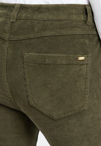 Olijf groene ribfluwelen broek met verticale ribbels, voorzien van een achterzak en een klein goudkleurig accent op de zak.