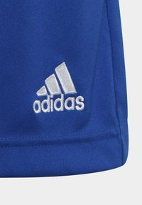 Pantalones cortos deportivos de tela azul que presentan un logo de Adidas bordado en blanco con un diseño de tres rayas. Textura suave y detalles de costura prácticos.