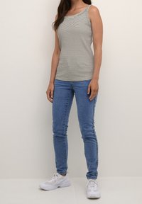 Gestreiftes ärmelloses Oberteil in Beige und Schwarz, kombiniert mit mid-blauen Skinny Jeans und weißen Sneakers. Glattes Material und figurbetontes Design.