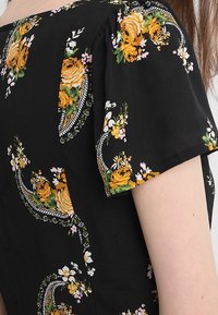 Svart blommig blus med gula och rosa blomster mönster, puffade korta ärmar och en strukturerad tyg med en slät finish.