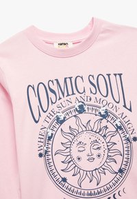 Lichtroze sweatshirt met lange mouwen en een marineblauw graphic met een lachende zon, de tekst "COSMIC SOUL" en hemelse ontwerpen rondom de zon.