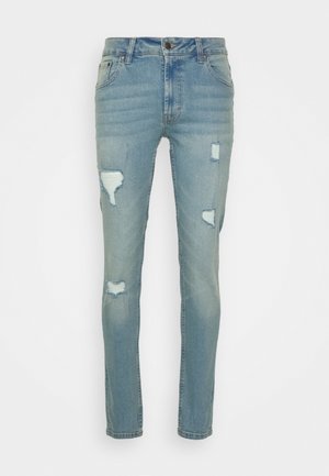 Jean en denim bleu au design ajusté, avec diverses déchirures et décolorations, style à cinq poches et fermeture à bouton à la taille.