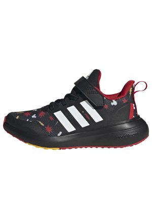 Scarpa sportiva nera con strisce bianche, dettagli rossi e tomaia in tessuto stampato con foglie multicolori. Cinghia sicura sopra i lacci.