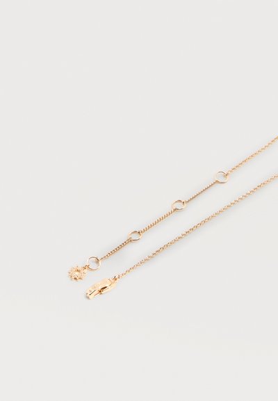 Λεπτό χρυσό κολιέ με μικρούς στρογγυλούς κρίκους και ένα μενταγιόν σε σχήμα ήλιου κοντά σε κούμπωμα, τοποθετημένο σε απλό λευκό φόντο.