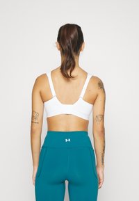 Hvit sports-bh med justerbare stropper og krok-og-løkke lukking, kombinert med teal høyt liv leggings med sidelommer.