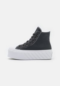 Czarne sneakersy typu high-top z syntetycznego materiału z białą gumową podeszwą. Posiadają szare sznurowadła i przeszycia; chropowata tekstura na podeszwie.
