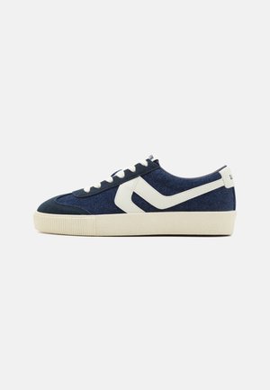 Navy canvas sneakers with white accents and laces. Textured rubber sole, featuring a logo on the back and a distinct triangular design element.