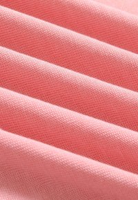 Tissu tricoté rose doux avec des mailles fines présenté en couches diagonales pliées pour le détail de la texture.