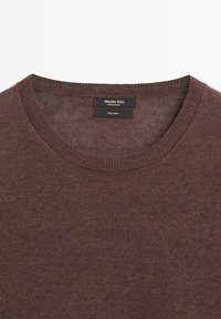 Pull en lin marron à col rond, avec une texture de maille fine et une étiquette de marque à l'intérieur. Design léger et simple.