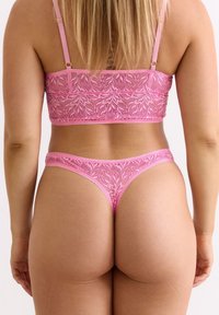 Roze kant bralette en thong set met een bloemenpatroon, voorzien van verstelbare bandjes en elastische randen voor een goede pasvorm. Zachte textuur en doorzichtige elementen.