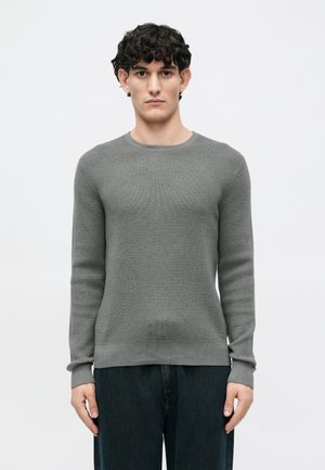 Pull en maille gris avec un motif texturé, col rond et manches longues. Associé à un pantalon sombre et ample.