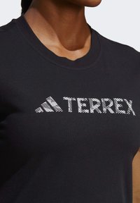 Černé tričko z bavlny s kulatým výstřihem. Na hrudi se nachází text "TERREX" v bílé, texturované grafice.