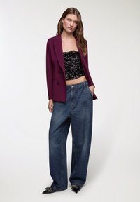 Blazer viola su misura sopra un top corto nero con paillettes, abbinato a jeans blu in denim dal taglio lungo e scarpe nere con punta e decorazioni.