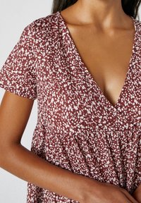 Vestido de tela con manchas rojas y blancas, de mangas cortas, escote en forma de V y cintura fruncida. La textura parece ligera y casual.