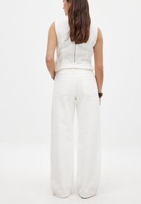 Biely textúrovaný crop top a široké nohavice, s bočným zipsom, jemnými vzormi a priliehavým pásom. Nohavice s zadnými vreckami.