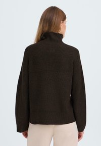 Brauner, gerippter Strickpullover mit hohem Kragen und langen Ärmeln, von hinten gezeigt. Das Design umfasst Raglanärmel und eine lockere Passform.
