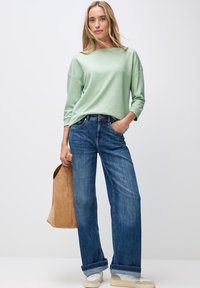 Mint grøn langærmet top, brede blå denim jeans, cremede sneakers og en tan ruskinds tote bag. Blødt stof, afslappet pasform, opkrøllede ærmer.