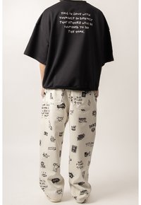 Czarny, oversize t-shirt z grafiką i cytatem na plecach, połączony z kremowymi spodniami z różnymi czarnymi wzorami w formie doodli.