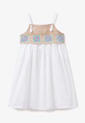 Robe blanche sans manches avec un yoke en crochet beige orné de motifs floraux bleus et roses, maintenue par deux boutons blancs sur les bretelles.