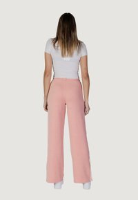 Pantaloni a gamba larga rosa chiaro con una finitura texturizzata e vita arricciata. Fessure laterali all'orlo e abbinati a un top bianco aderente.