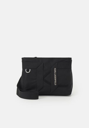 Czarna prostokątna torba na ramię z regulowanym paskiem, srebrnym pierścieniem i logo "KARL LAGERFELD" na przodzie.