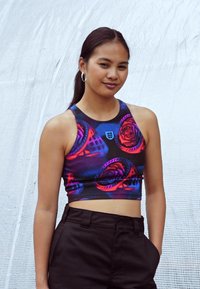 Flerfarget kort tanktopp med blomsterdesign i lilla og rosa mot en svart bakgrunn, kombinert med høyt liv svarte bukser.