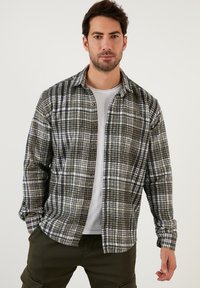 Kockás flaneling zöld, fekete és fehér színekben. Hosszú ujjakkal, gombos záródással és laza szabással rendelkezik, puha textúrával.