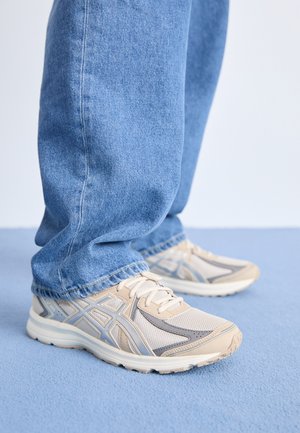 Baskets de sport beiges avec des empiècements en mesh et en synthétique, ornées d'accents gris et d'une semelle texturée. Portées avec un jean en denim bleu clair.