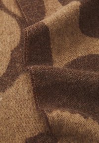 Brown and beige patterned fabric with a soft texture, featuring irregular shapes in a wool-like material. Edges have visible stitching.
