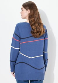 Blå tröja med ribbad textur, prydd med vågiga ränder i röd, vit och marinblå. Långa ärmar och avslappnad passform. Bakvy visas.