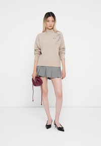 Maglione beige lavorato a maglia con applicazioni floreali, gonna grigia plissettata, scarpe col tacco nere a punta e una borsa a tracolla bordeaux.