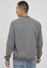 Grå hettegenser med ribbestrikket krage og mansjetter, som har en myk tekstur og et enkelt design. Vist fra baksiden, brukt med lyse jeans.