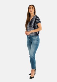 Top de rayas en azul marino y blanco de manga corta, combinado con jeans ajustados de un azul claro y tacones negros de punta. Tejido suave y diseño entallado.