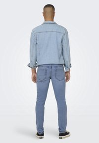 Chaqueta de mezclilla azul claro con un corte relajado, combinada con jeans azul claro. La chaqueta cuenta con bolsillos clásicos y una textura suave.