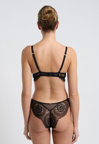 Bralette de encaje negro con tirantes ajustables y patrones florales intrincados; braguita de encaje transparente a juego con bordes festoneados y acentos.