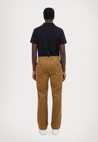 Schwarzes Poloshirt, braune Cordhosen mit glatter Textur, gerades Bein-Design und zwei Gesäßtaschen, getragen mit weißen Sneakers.