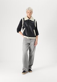 Melnas ādas veste ar krēmkrāsas vilnas akcentiem un apkakli, apvienota ar pelēkām platām biksēm un melniem sneakers ar gumijas zole.