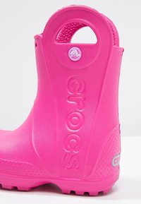 Botte en caoutchouc rose imperméable avec une surface texturée, un bout arrondi, un accent de logo et une poignée latérale pour un enfilage facilité.