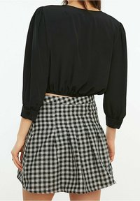 Blusa nera cropped con maniche a puff abbinata a una gonna plissettata grigio e nera a quadri. Tessuto liscio con dettagli a bottoni sulle maniche.