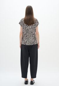Camicia a maniche corte a righe beige e nere abbinata a pantaloni neri larghi. Scarpe nere visibili in basso.