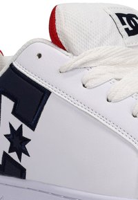 Vit sneaker med marinblå accenter, med en strukturerad läderöverdel, stjärn- och diamantformer, vita snören och röd detaljer på tungan.