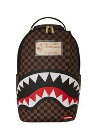 Mochila a cuadros marrón con un diseño de boca de tiburón en blanco y rojo, con detalles en dorado y una etiqueta en la parte frontal.
