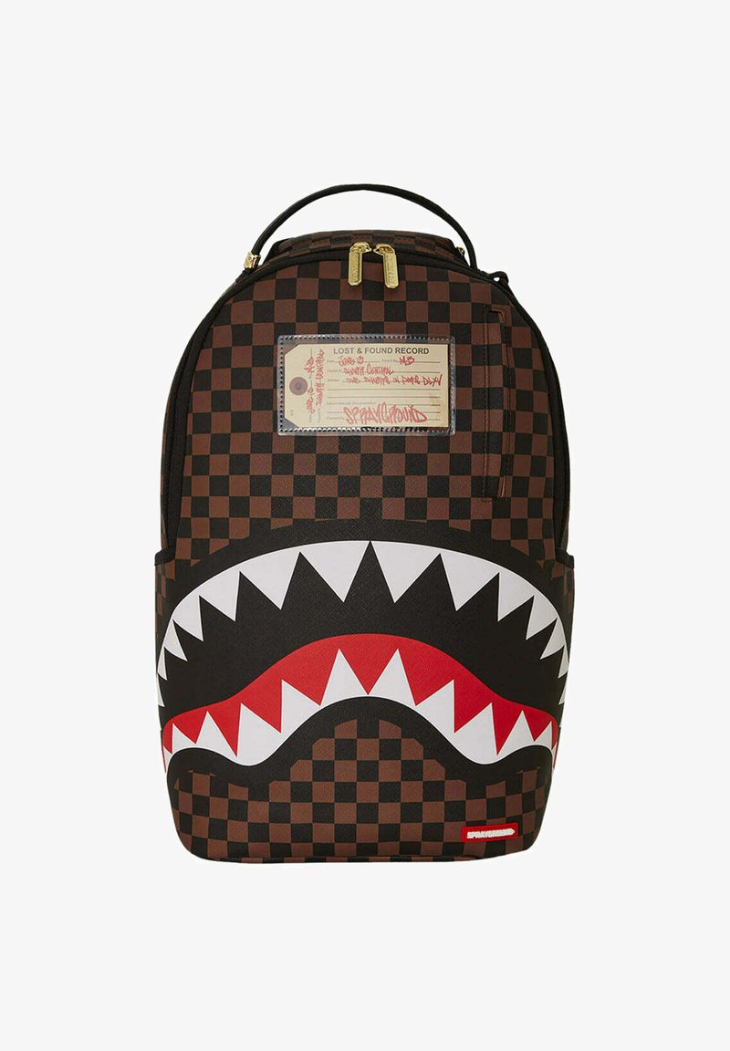 Mochila a cuadros marrón con un diseño de boca de tiburón en blanco y rojo, con detalles en dorado y una etiqueta en la parte frontal.