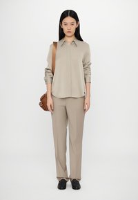 Beige long-sleeve shirt with a pointed collar, paired with matching tailored trousers. Brown crossbody bag and black shoes complete the look.