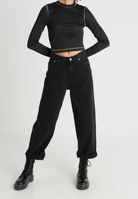 Zwarte cropped lange mouwen top met zilveren stiksel, gecombineerd met zwart hoog-was denim, opgerolde manchetten en zwart veterschoenen met een chunky zool.