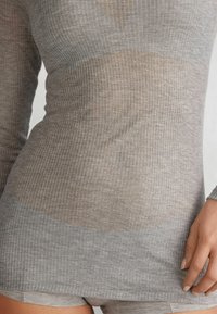 Šedý top s dlouhým rukávem, ribbed designem, který má poloprůhlednou texturu, přiléhavý střih a kulatý lem. Materiál vypadá lehce a mírně texturovaně.