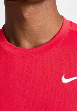 Zbliżenie na osobę noszącą czerwoną koszulkę Nike z białym logo Nike swoosh na prawym biodrze.