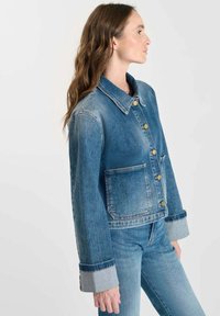 Jeansjacka med en klassisk design, med en spridd krage, knappar fram och en bröstficka. Ljusblå färg med en blekt textur.