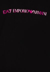 Camiseta negra con el texto "EA7 EMPORIO ARMANI" en un vibrante color rosa, con una fuente moderna y elegante y una textura de tela suave.